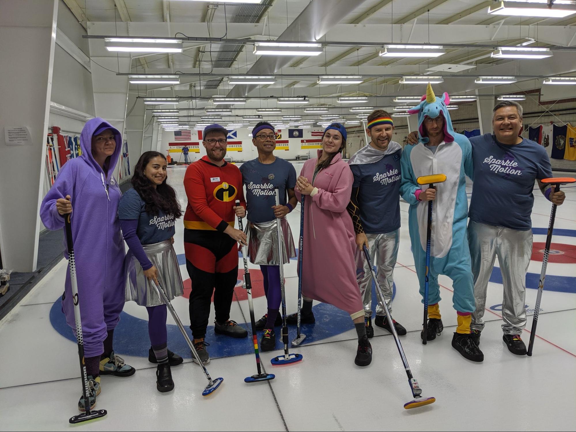 A photo of two teams on curling ice, some dressed up and some in matching outfits.
